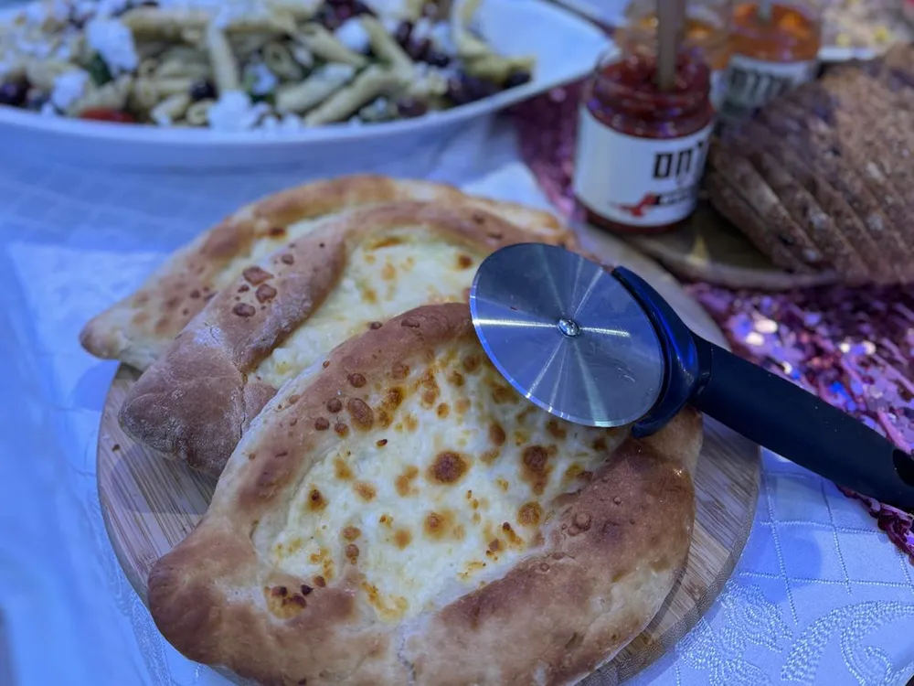 חצ'פורי בצורת סירה ממולא גבינה על קרש עץ, לצד סלט פסטה, לחם וצנצנות רוטב על שולחן בופה באירוע